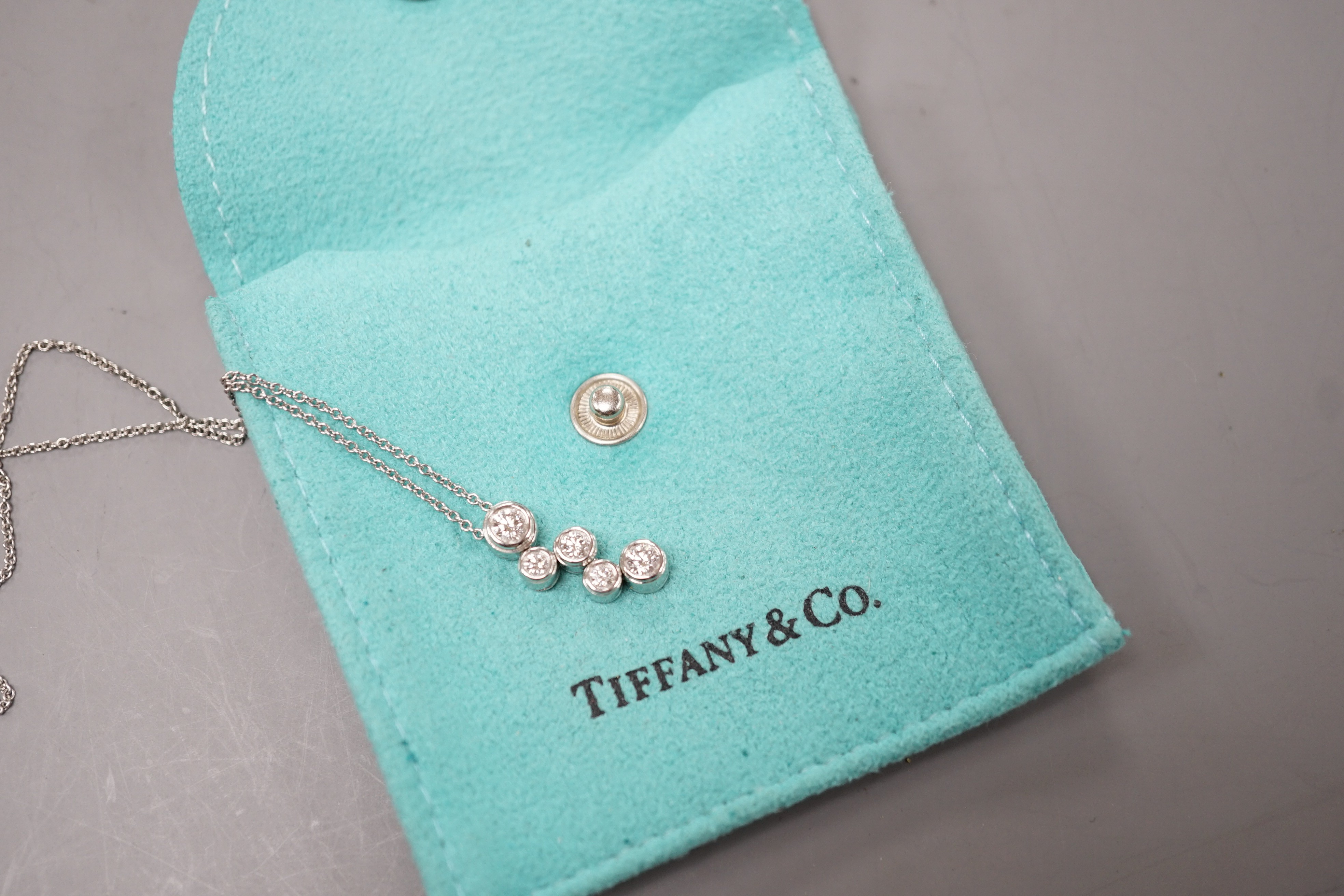 A modern Tiffany & Co platinum and graduated five stone diamond cluster set pendant necklace, pendant 18mm, chain 40cm, gross weight 5.2 grams, with Tiffany pouch.